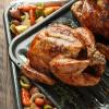 Whole roasted chicken on a roasting pan with carrots, potatoes, celery and onions