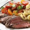 A thin sliced medium sirloin with sides of califlower and halved Roma tomatoes.