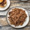 Pulled beef on a plate and bun with a side of BBQ sauce