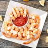 Shrimp on a square white plate with lemon and cocktail sauce