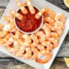 Shrimp on a square white plate with lemon and cocktail sauce